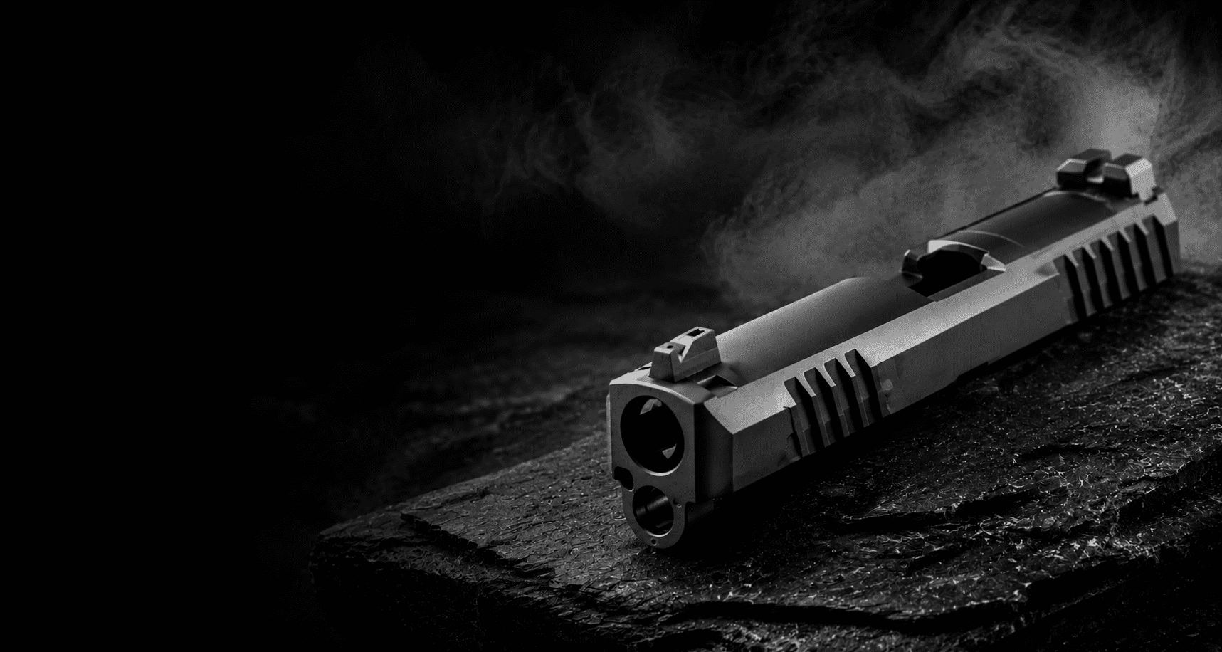 Dark cinematic hero image featuring a precision-machined SIG Sauer pistol slide on a rugged stone surface with smoke effects.